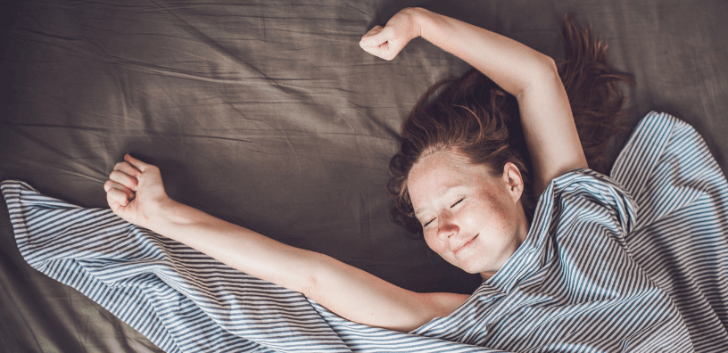 A young girl stretches happily in cool, cozy bedding as the sun rises.