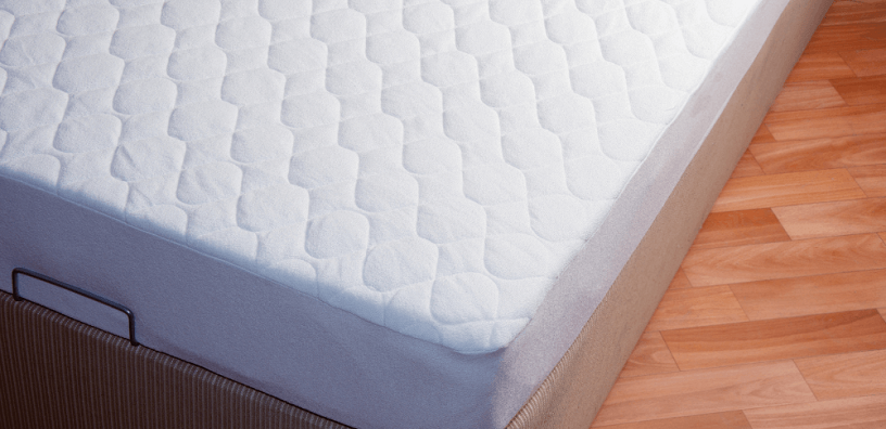 A neatly arranged bed with a mattress protector on top.