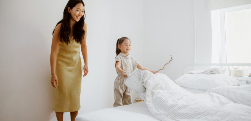 A woman and her kid are fixing their bed.