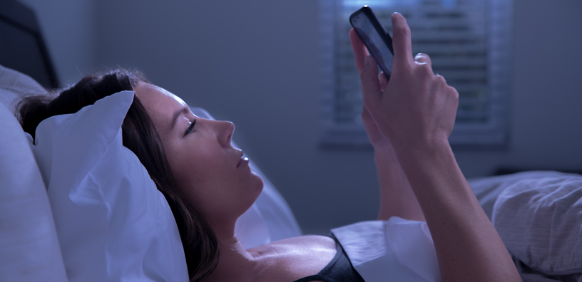 A woman viewing her cellphone while trying to sleep.