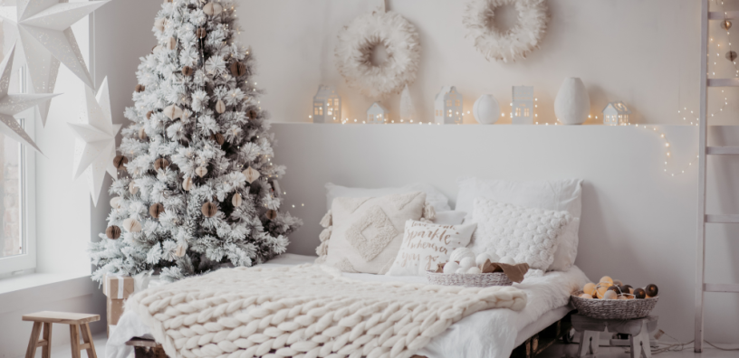 A well arranged bed with a Christmas tree beside it.