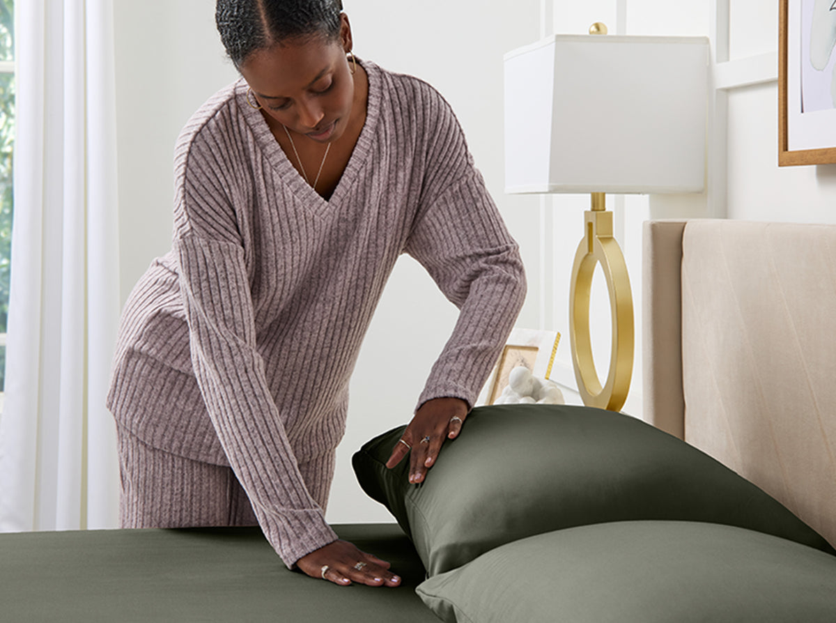 Woman arranging grey bamboo pillows on a bed in a well-lit room
