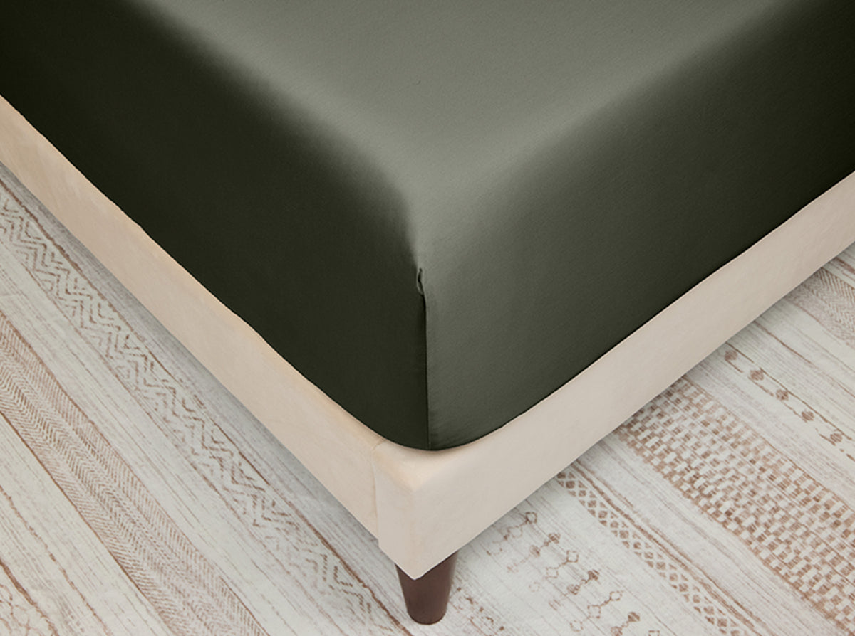 Grey fitted sheet on a bed with a light wooden floor and patterned rug.