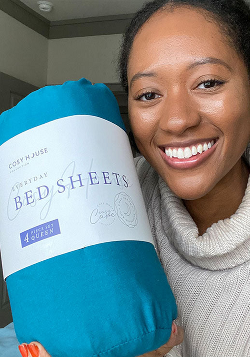 Another happy female customer is holding a packaged set of Cosy House Collectionâs Everyday Bed sheets.