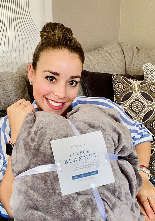 A customer is comfortably sitting down to show her Everyday Fleece Blanket.