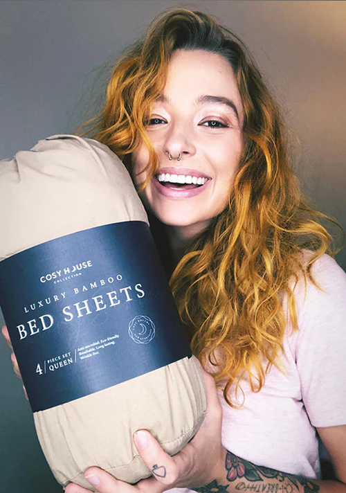 A happy customer is holding a packaged set of Cosy House Collectionâs Luxury bed sheets.