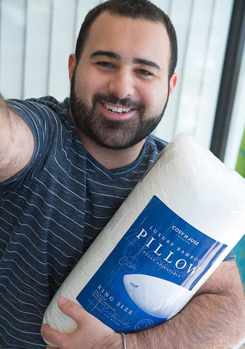 A happy male customer is holding a packaged Cosy House Collection Luxury pillow.