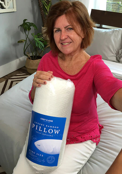 A female customer sitting on the bed is holding a packaged Cosy House Collection Luxury pillow.