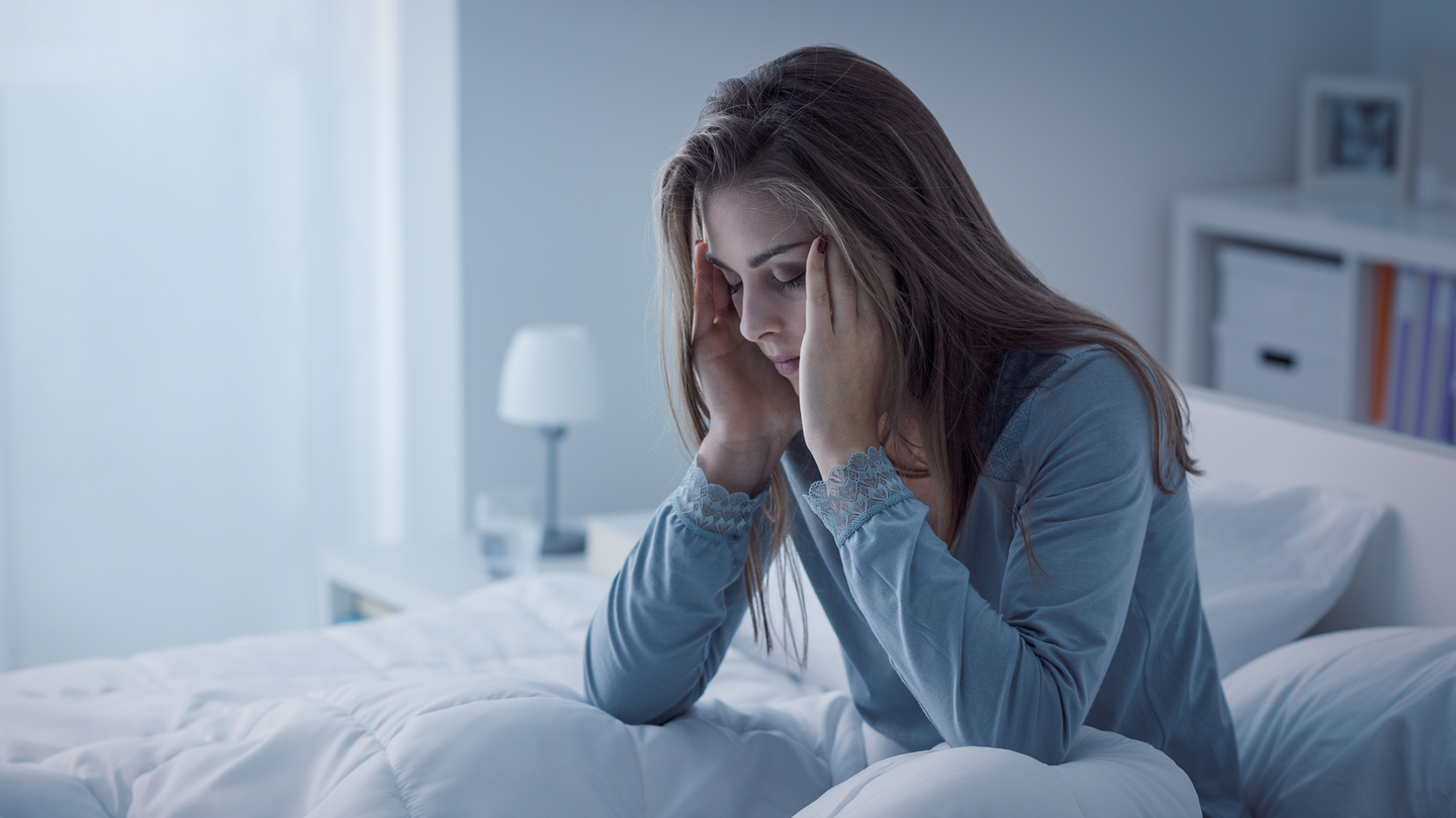 A woman sitting on the bed seems to be having a headache.