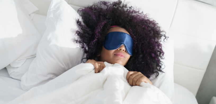 A woman relaxing in bed, wearing a blue eye mask, enjoying a moment of peace and tranquility.