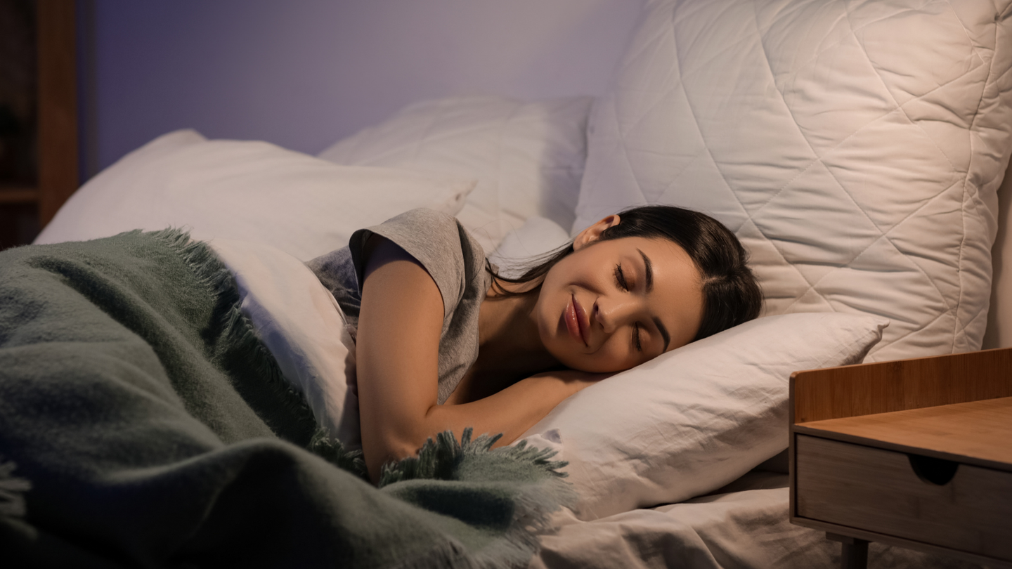 Peaceful woman sleeping on a white bed with a sage green fleece blanket — using calming textures to support restful sleep