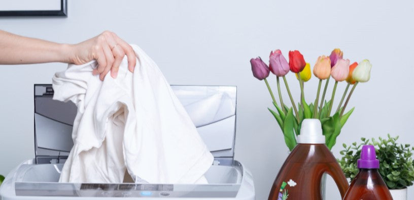 A hand is dropping laundry into the washing machine.