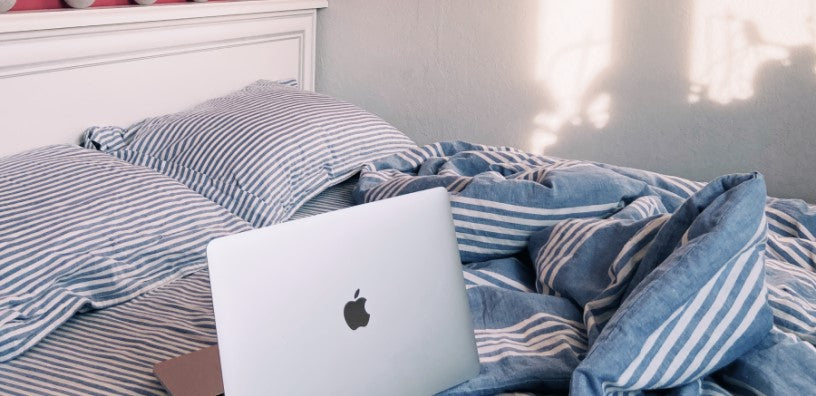 A MacBook is on top of a disheveled bed.