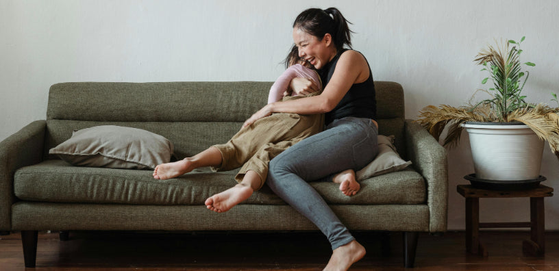 A young mother lovingly and playfully hugs her young son on their couch at home.