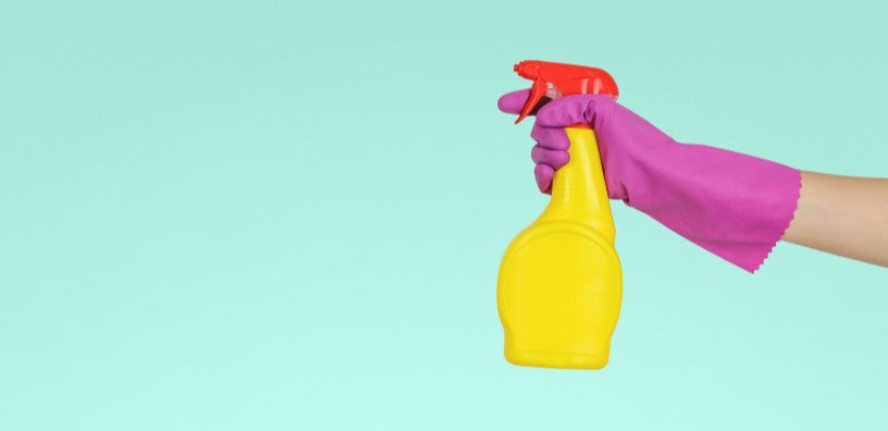 A hand covered in a latex glove is holding a spray bottle.