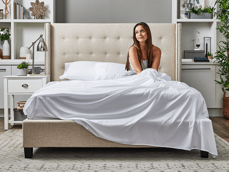 A woman is seated on a bed with Cosy House Collection bedding, exuding a sense of relaxation and tranquility.