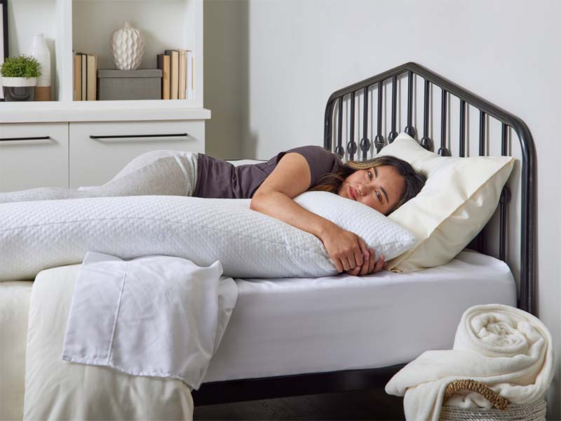 A woman peacefully resting on a cozy bed, hugging a Cosy House Collection Luxury Body Pillow.