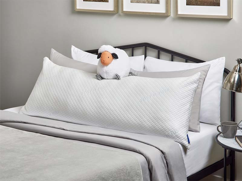 A neatly arranged bed with Cosy House Collection bedding. There is also a fluffy stuffed animal resting on the Luxury Body Pillow.