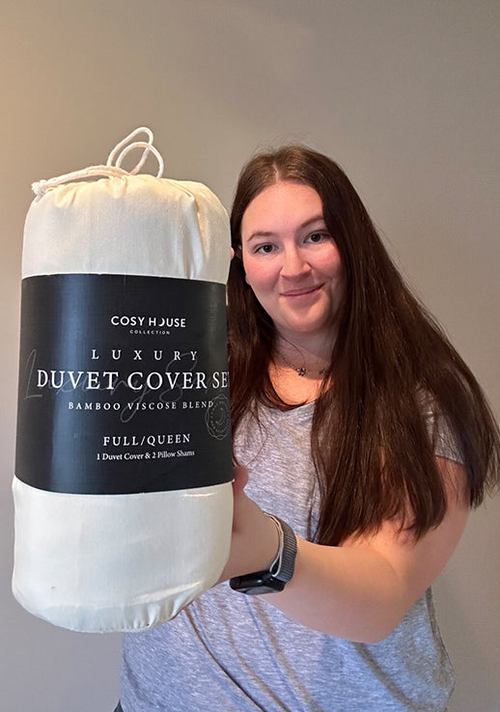 A standing and smiling customer flexes her packaged Luxury Duvet Cover set.