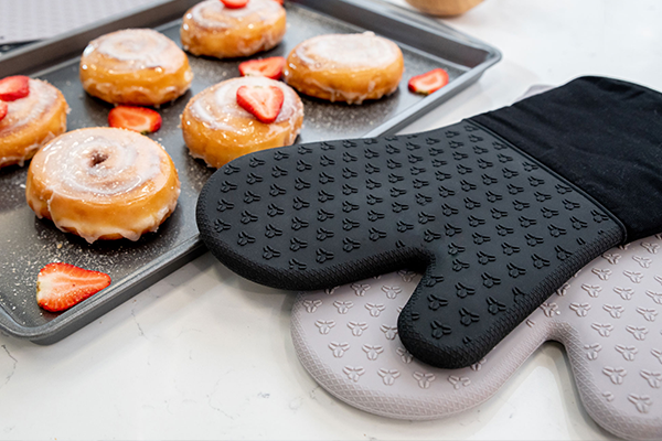 A baking tray filled with delicious donuts next to a pair of oven mitts.