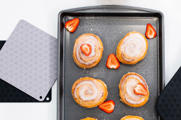 A baking tray filled with delicious donuts next to a pair of pot holders.