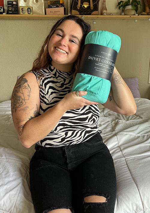 A customer is comfortably sitting down on her bed displaying her new Luxury Duvet Cover set.