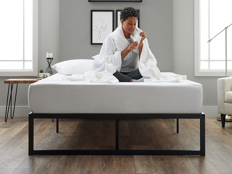 A woman is seated on a bed with Cosy House Collection bedding, exuding a sense of relaxation and tranquility.
