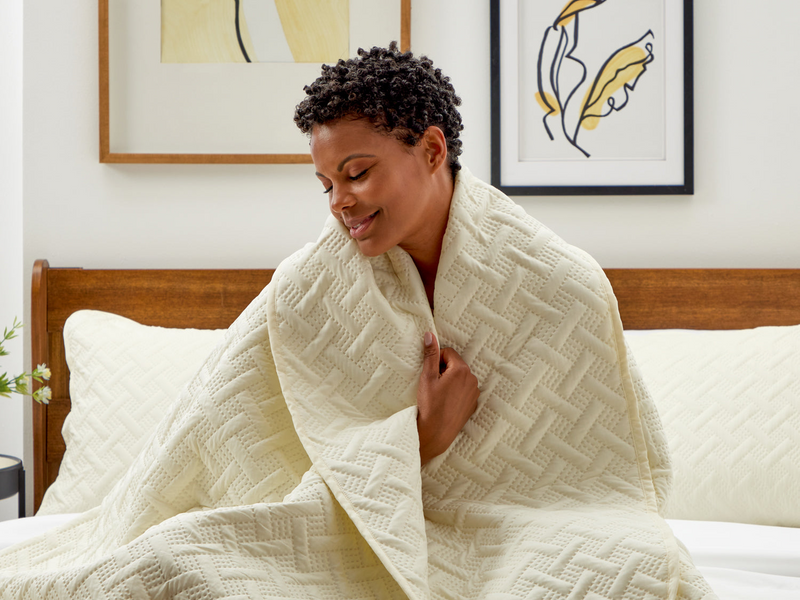 A woman wrapped in a Cosy House Collection Luxury Quilt, enjoying a peaceful moment on her bed.